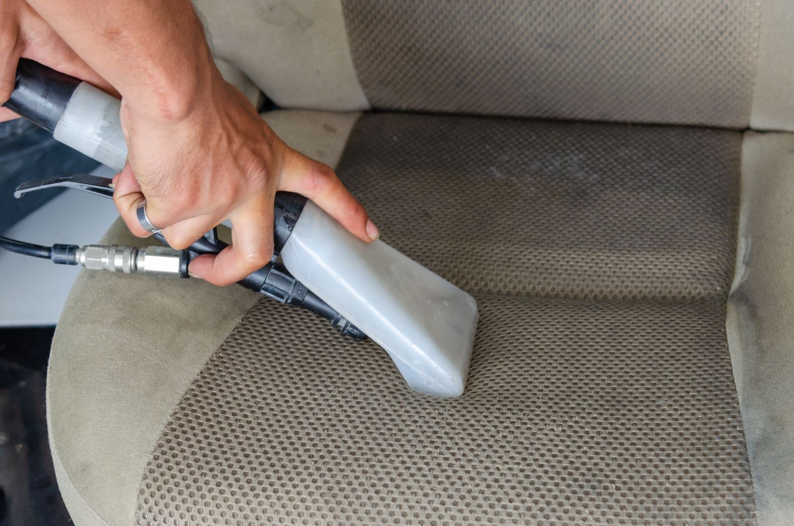 Overhead close-up of a hand using a vacuum crevice tool on a fabric car seat