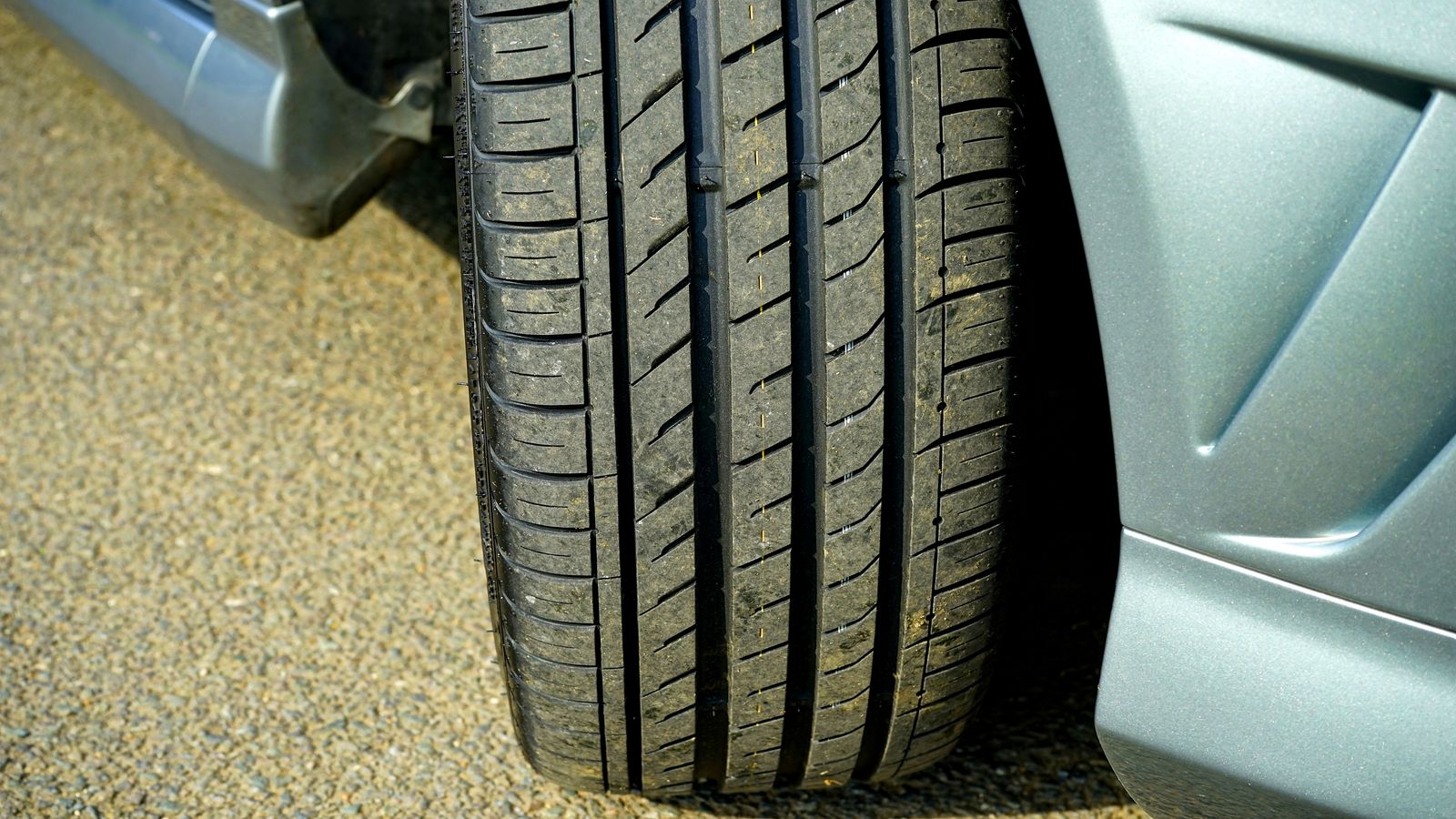 Close-up of a car tire and wheel arch on gravel