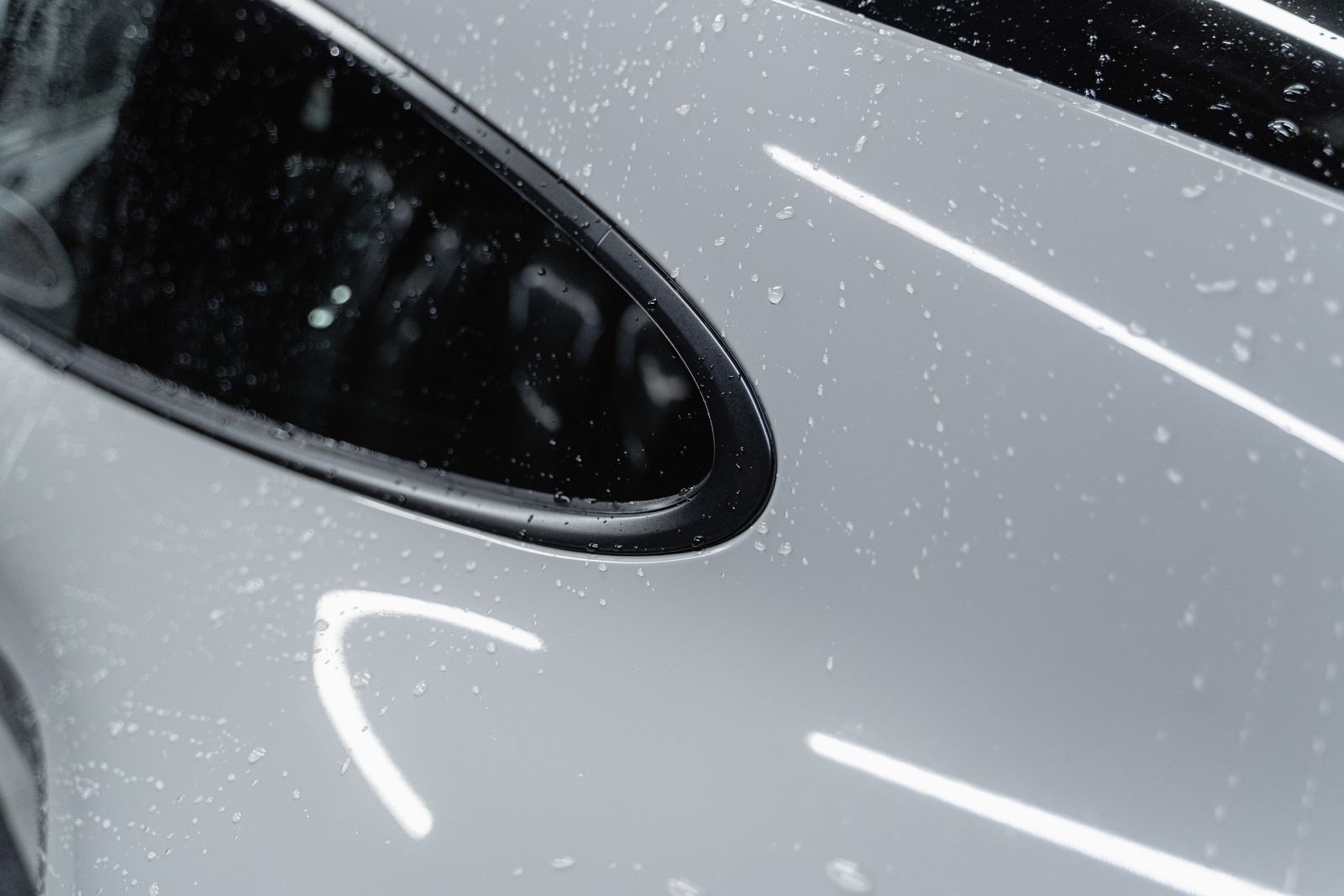 Extreme close-up of water droplets beading on a light-grey car's door and window-trim area after a wash